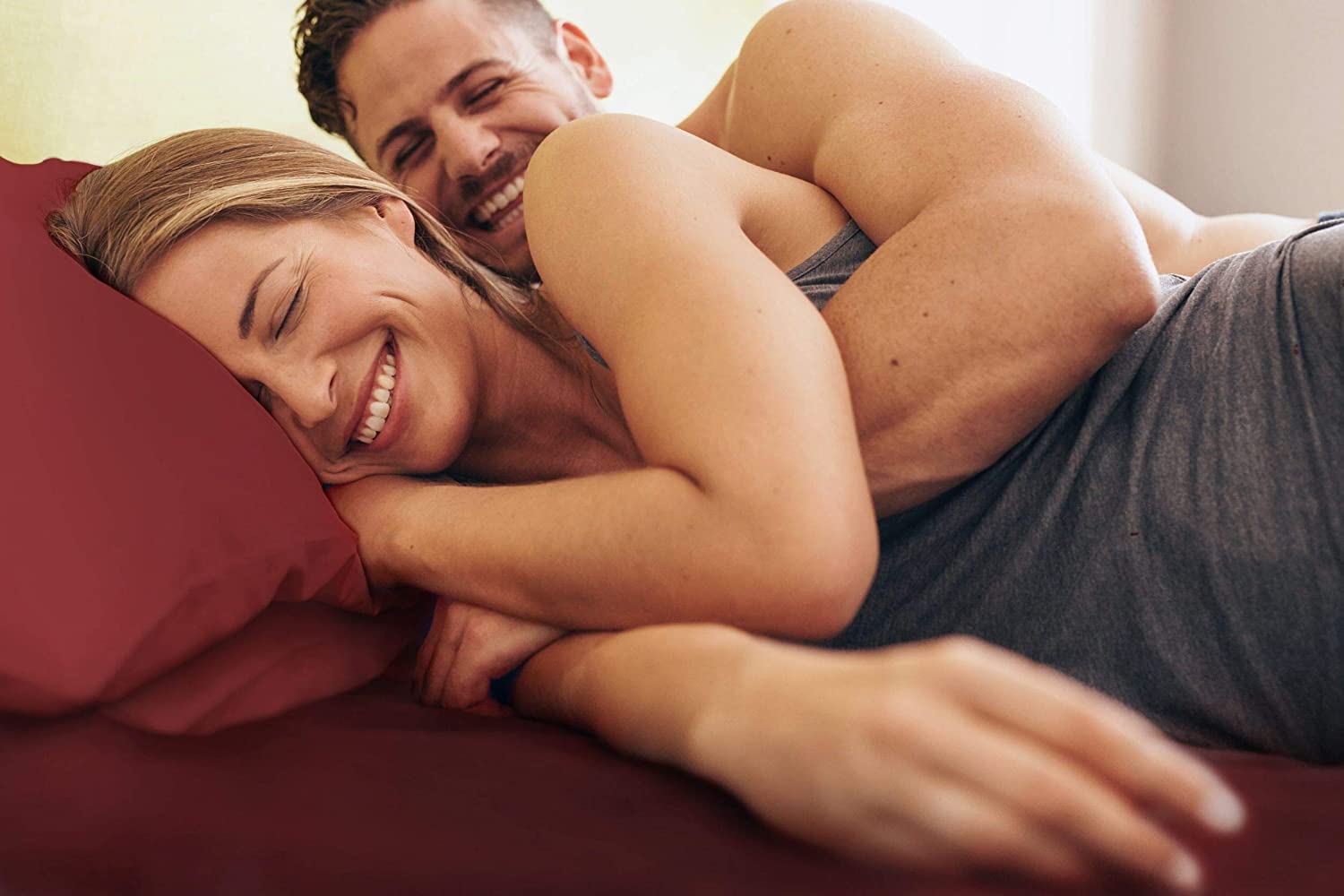 Man and woman laying in bed with burgundy sheets