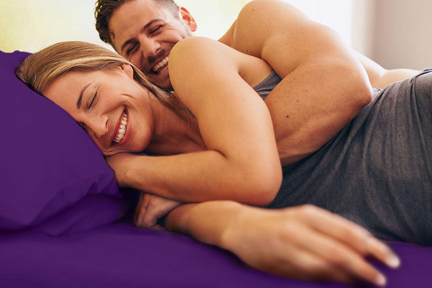 Man and woman laying in bed with purple sheets